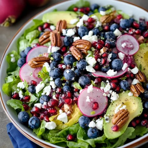 A bowl of salad with blueberries, avocado, and pecans.