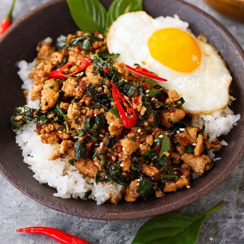 A bowl of Thai Basil Chicken with rice and a fried egg on top.