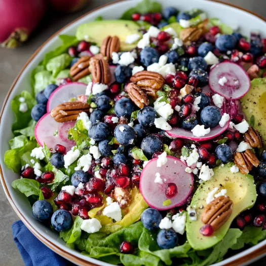 A bowl of salad with blueberries, avocado, and pecans.