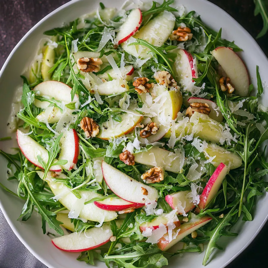 A bowl of salad with apples, spinach, and walnuts.
