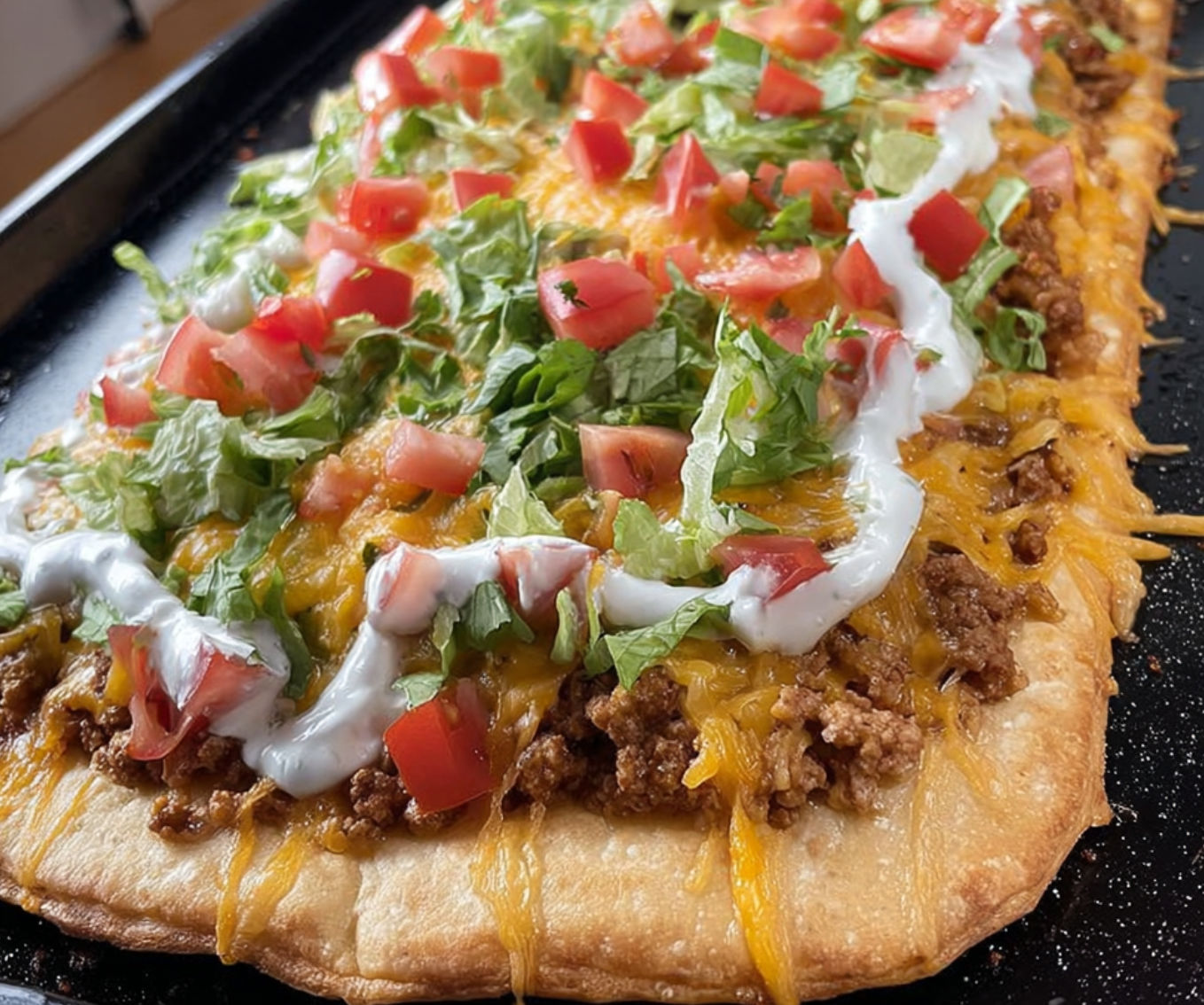 A delicious Taco Pizza with a variety of toppings, including tomatoes, lettuce, and cheese, is ready to be enjoyed.