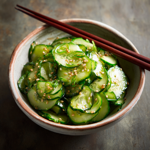 A bowl of cucumber salad with sesame seeds and chopsticks.