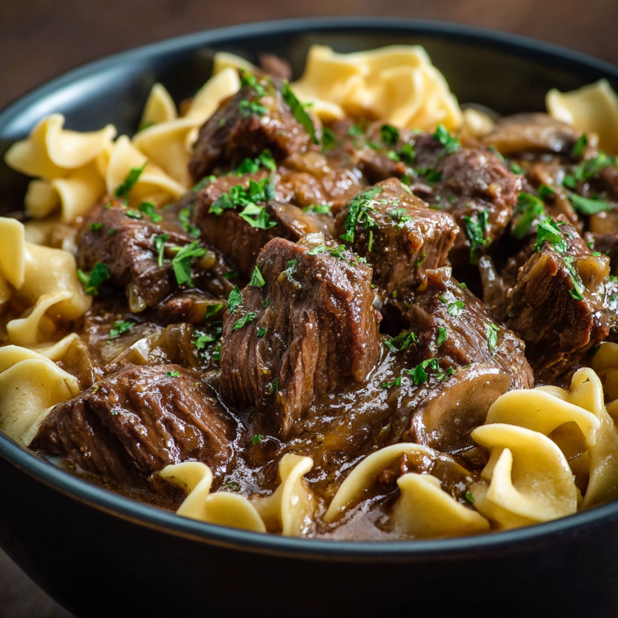 A bowl of beef stew with noodles, mushrooms, and herbs.