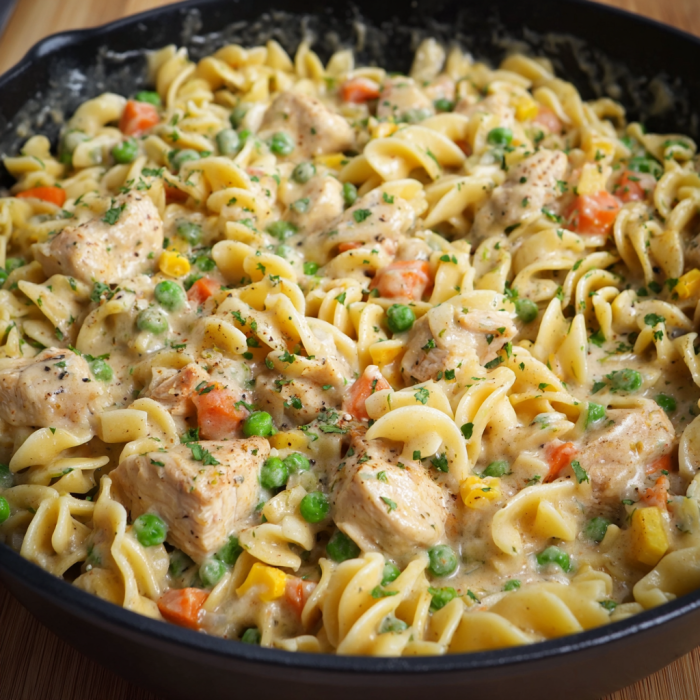 A delicious pasta dish with chicken, peas, and carrots, served in a black bowl.
