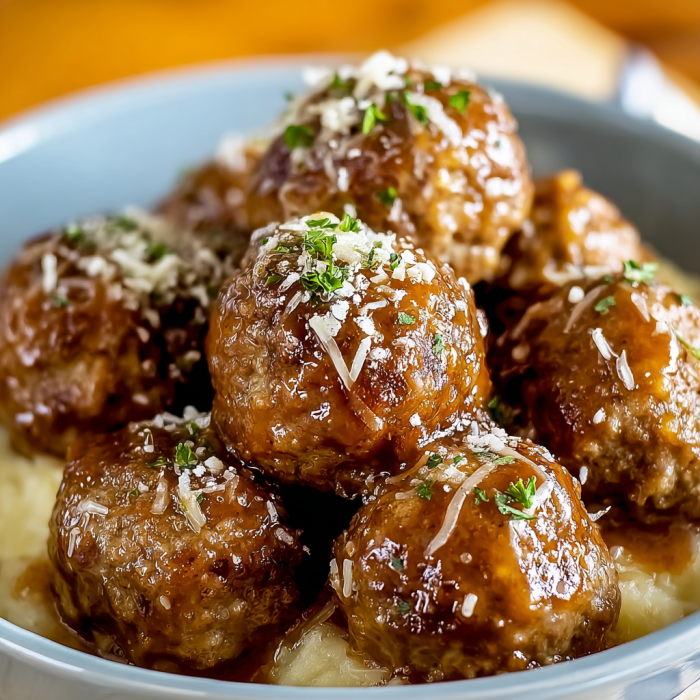 A bowl of meatballs covered in a brown sauce, served with a side of pasta.