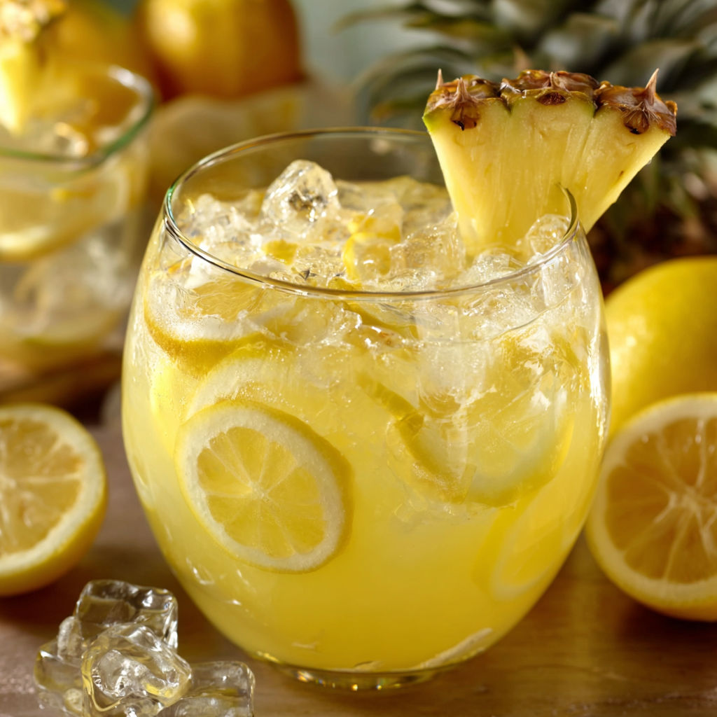 A glass of Pineapple Lemonade Punch is filled with lemon slices and pineapple chunks, creating a refreshing and tropical beverage.