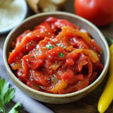 A bowl of red sauce with peppers and tomatoes.