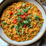 A bowl of food with a variety of vegetables and herbs, including tomatoes, peppers, and parsley.