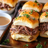 A tray of sandwiches with meat and cheese on a pan.