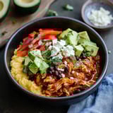 A bowl of food with chicken, beans, and avocado.