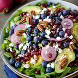 A bowl of salad with blueberries, avocado, and pecans.