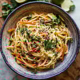A bowl of pasta with vegetables and sauce.
