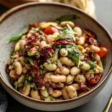 A bowl of food with tomatoes, beans, and lettuce.