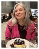 A woman is sitting at a table with a plate of food in front of her. The plate contains a dessert with berries on top.