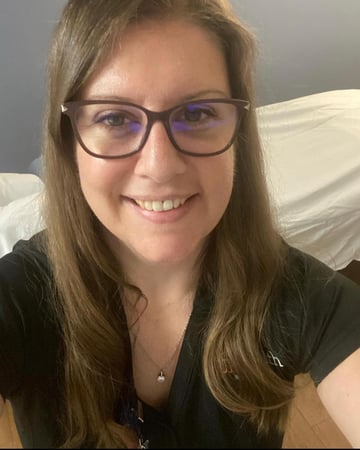 A woman wearing glasses and a black shirt is smiling at the camera.