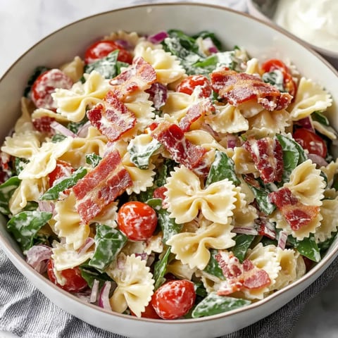 A bowl of pasta salad with tomatoes, spinach, and bacon.