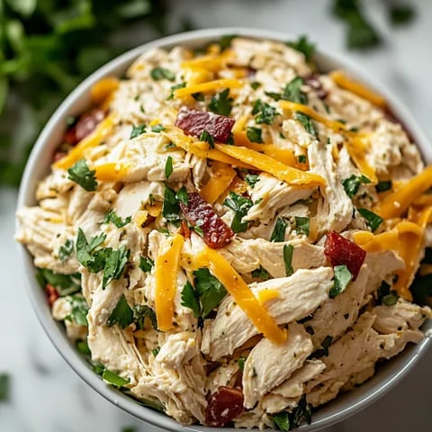 A bowl of chicken salad with cheese and tomatoes.