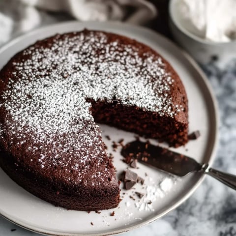 A slice of chocolate cake with powdered sugar on a plate.
