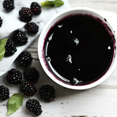 A cup of blackberry juice with a few blackberries on the side.