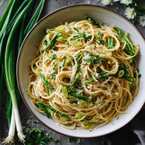 A bowl of Lemon Garlic Scape Pasta with a fork and a knife nearby.