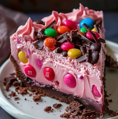 A slice of Pink M&M Snickers Cheesecake on a white plate.