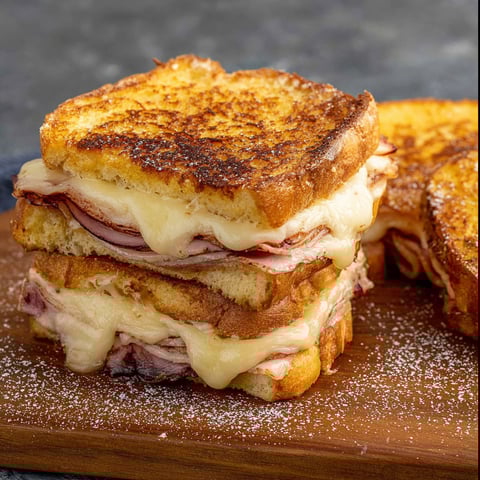 A stack of Monte Cristo sandwiches on a wooden cutting board.