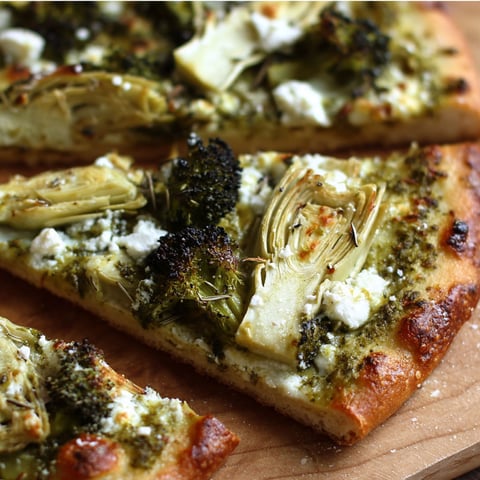 A slice of pizza with broccoli, feta, and pesto on a wooden cutting board.
