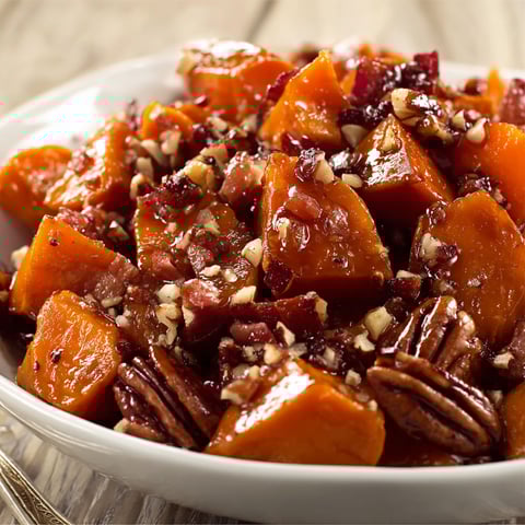 A white bowl filled with candied yams, pecans, and bacon.