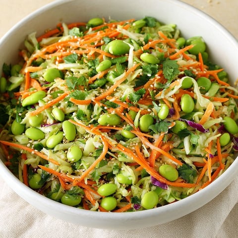 A bowl filled with a salad containing carrots, green beans, and edamame.