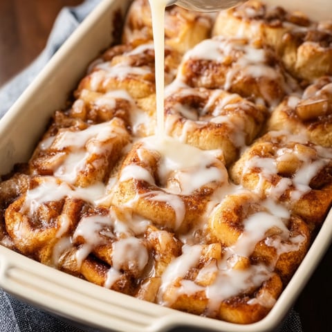 A delicious dessert, the 2 Ingredient Apple Cinnamon Roll Bake, is being prepared in a white bowl.