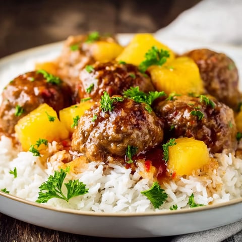 A plate of Sweet and Sour Meatballs with rice and pineapple chunks.