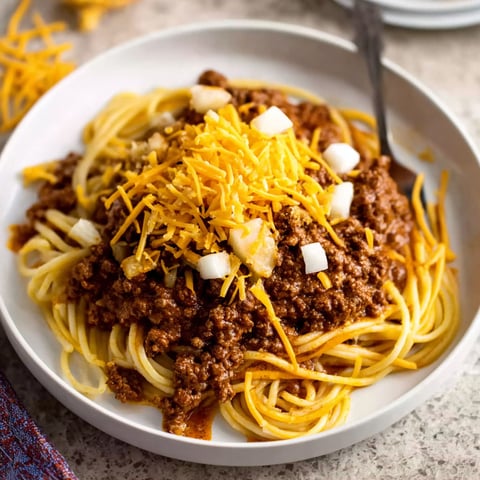 A plate of Cincinnati Chili with cheese and onions on top.