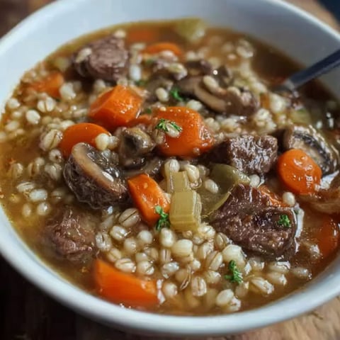 A bowl of beef and barley soup with a spoon in it.