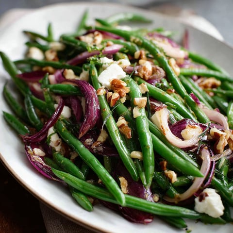A plate of green beans with onions, nuts, and feta cheese, served as a salad.