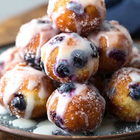 A plate of baked blueberry fritter bites with a drizzle of icing on top.