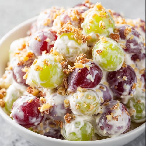 A bowl of creamy grape salad with a variety of grapes and nuts.