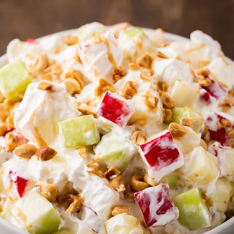 A bowl of Taffy Apple Salad, topped with walnuts and a drizzle of caramel, is ready to be enjoyed.