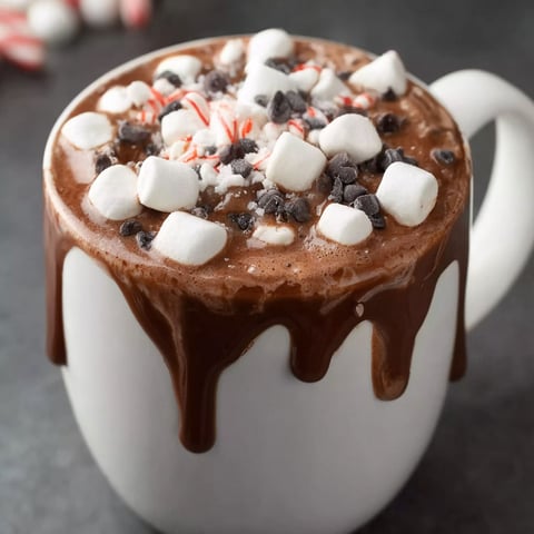 A cup of hot chocolate with marshmallows and chocolate drizzled on top.