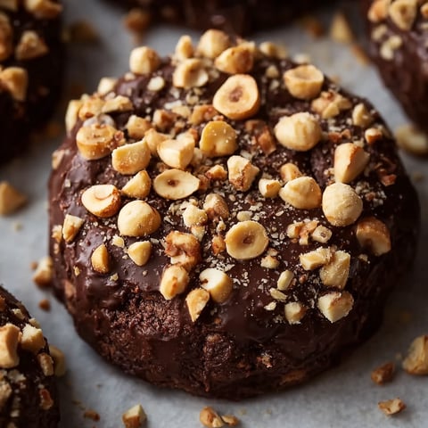 A close up of a chocolate hazelnut crunch cookie with chopped hazelnuts on top.