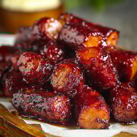 A delicious and mouth-watering dish of Sticky Sweet Baked Hot Dog Burnt Ends, served on a wooden platter.