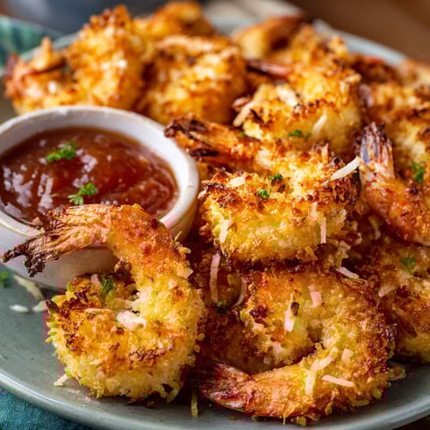 A plate of air fryer coconut shrimp with a dipping sauce.