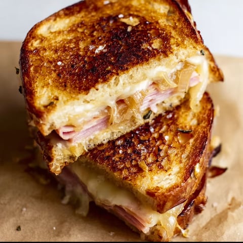 A sandwich with Gruyere, caramelized onions, sage, and ham is displayed on a table.