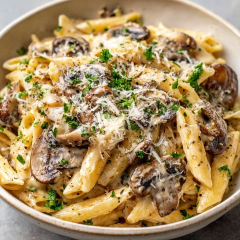 A bowl of pasta with mushrooms and cheese, served with a side of greens.