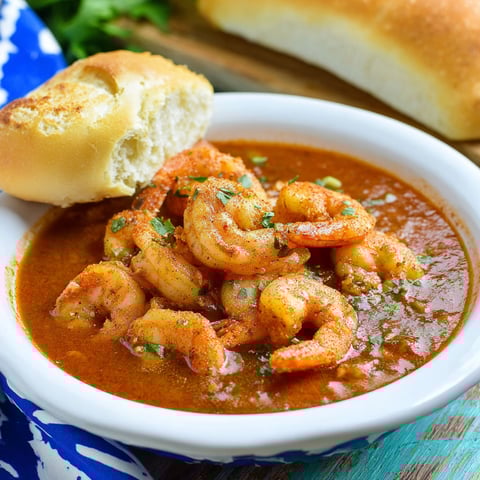 A bowl of shrimp soup with a piece of bread on the side.